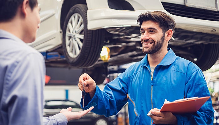 Smiling service technician holding a clipboard and returning car keys to a customer